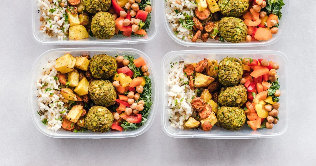 Cuatro táperes de meal prep con arroz, verduras asadas y falafel, vistos desde arriba